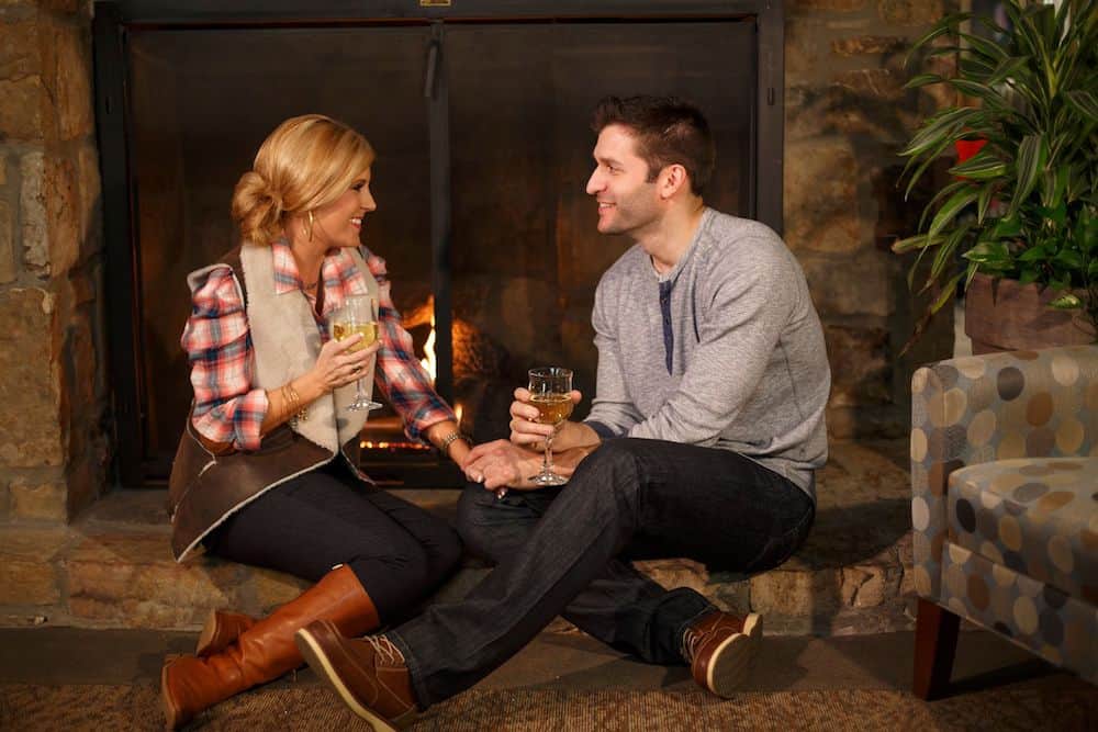 couple sitting next to fireplace with drinks